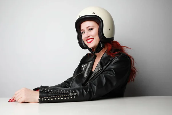Feliz jovem motociclista mulher usa capacete e jaqueta de couro posando sobre parede branca. — Fotografia de Stock