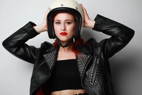 Foto da jovem mulher motociclista usa capacete e jaqueta de couro posando na parede branca. — Fotografia de Stock
