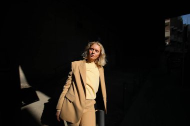 Havalı bej takım elbiseli, sarı saçlı, modaya uygun genç bir bayan model..