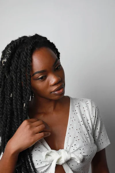 Mulher africana jovem atraente com tranças posando sobre a parede branca. Vertical. — Fotografia de Stock