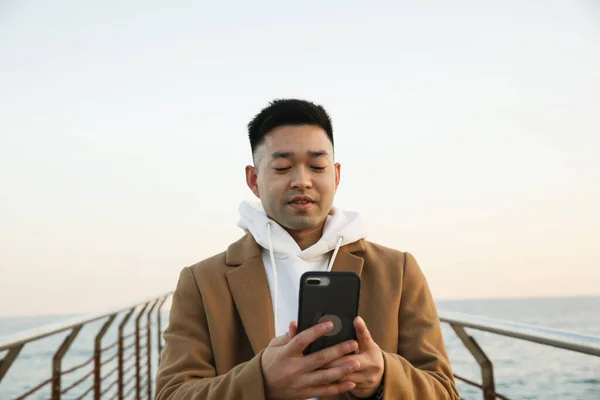 Kumsalda akıllı telefonunu kullanan yakışıklı bir Asyalı. Serbest konsept. — Stok fotoğraf