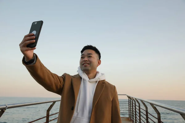 Portret van de jonge Aziatische man met behulp van zijn smartphone op het strand. — Stockfoto