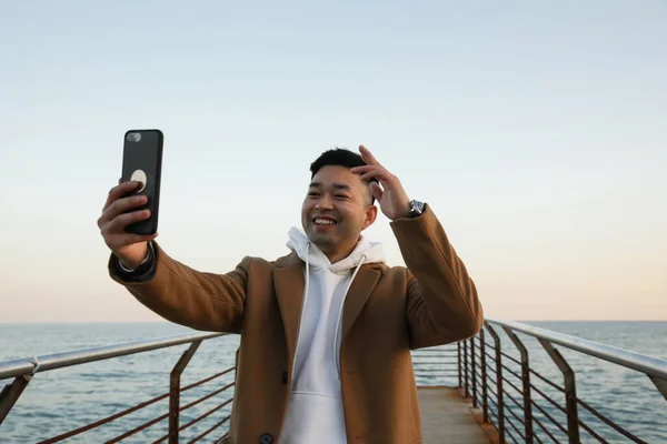 Jonge Aziatische man lacht en gebruikt zijn smartphone op het strand. Freelance. — Stockfoto