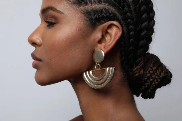 Close-up of African young woman with braids and earrings posing on grey wall. — Stock Photo, Image