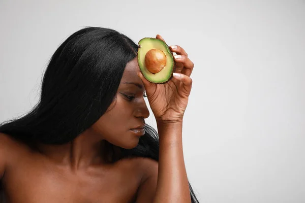 Portrait of black young woman holds half-part of avocado posing on white wall. — Stock Photo, Image