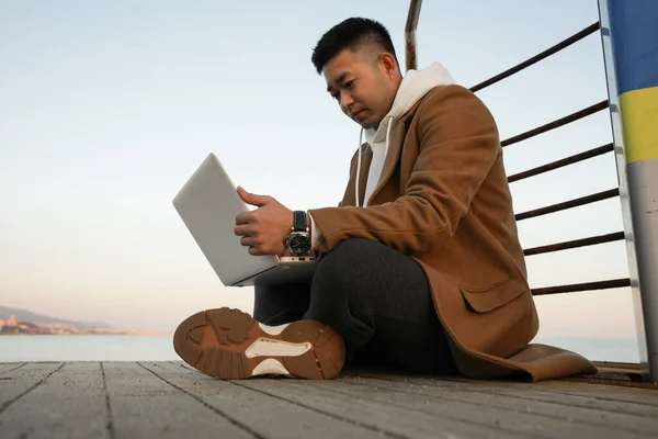Ontspannen jonge Aziatische man met behulp van laptop op het strand. — Stockfoto