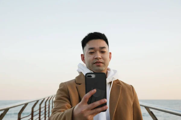 젊은 아시아 청년 이 해변에서 스마트폰을 사용하고 있습니다. 프리랜서와 사업. — 스톡 사진