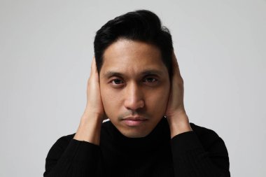 Asyalı adam kulaklarını kapatıyor ve kameraya bakıyor. Ruh sağlığı sorunları. 