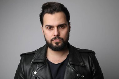 Sakallı yakışıklı genç adam, beyaz arka planda deri ceketli poz veriyor..