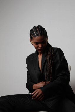 Uzun örgülü Afrikalı genç bir kadının dikey portresi koyu renk süit giyiyor.