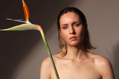 Güzel, esmer, genç bir kadın evde egzotik çiçeklerle poz veriyor.. 