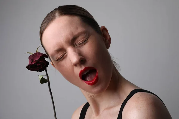 Молода жінка з сухою трояндою та емоційним виразом обличчя позує на білій стіні . — стокове фото