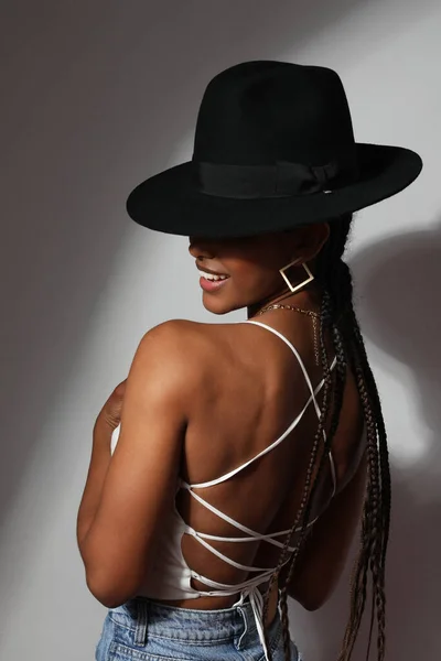 Весела африканська молода жінка з плечима носить чорний капелюх, що стоїть у приміщенні. Вертикальний — стокове фото