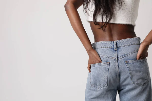 Mock-up van jonge zwarte vrouw dragen blauwe jeans en top geïsoleerd op grijze muur. — Stockfoto