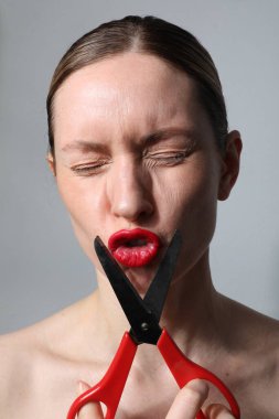 Makas tutan kadın kameraya bakıp beyaz arka planda poz veriyor. Dikey.