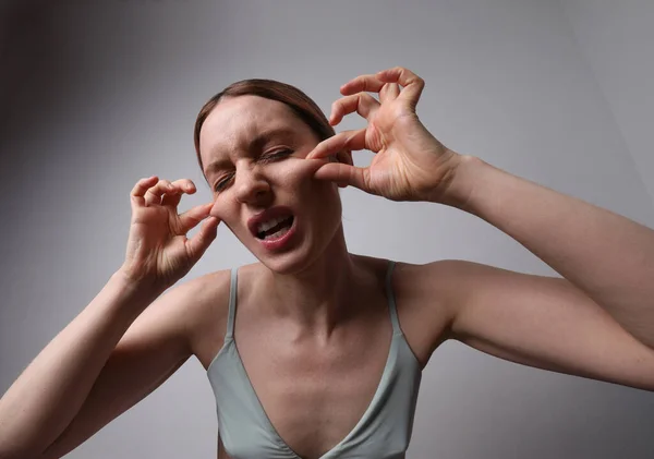 Молода жінка торкається її обличчя, роблячи масаж обличчя позує на білій стіні . — стокове фото