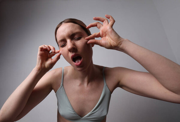 Middle aged woman touching her face doing a lift massage posing on white wall.