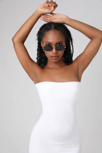 Fiatal afro-amerikai nő fehér ruhát visel pózol beltéri fehér fal. — Stock Fotó