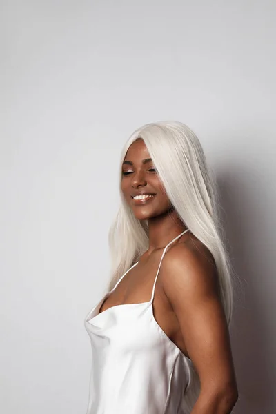 Smiling African American young woman with long blond hair and white dress. — стокове фото