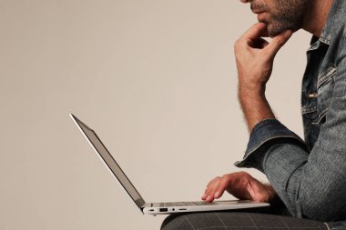 Beyaz arka planda tek başına otururken dizüstü bilgisayarla çalışan traşsız bir adamın kesilmiş portresi.