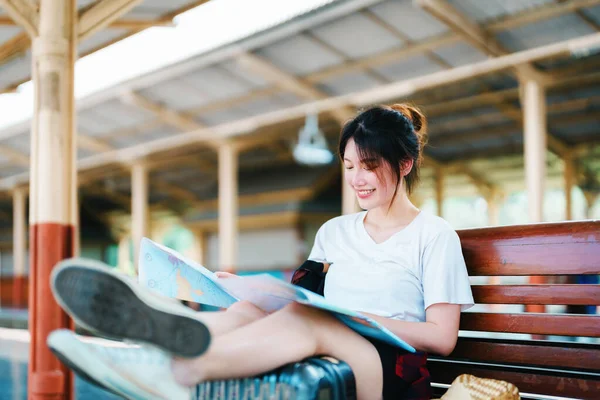 Summer, relax, vacation, travel, portrait of a cute Asian girl looking at a map to plan a trip while waiting at the train station. — Zdjęcie stockowe