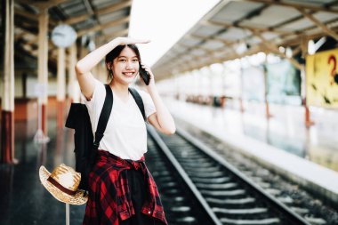 Yaz, dinlenme, tatil, seyahat, güzel Asyalı kızın portresi tren istasyonundaki arkadaşlarını aramak için akıllı telefonu kullanıyor..
