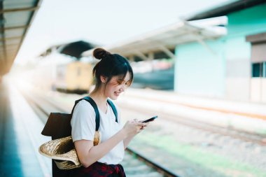 summer, relax, vacation, travel, portrait of beautiful Asian girl using the smartphone mobile to call friends at the train station while waiting for their travel time.