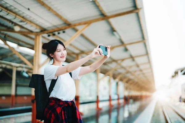 Summer, relax, vacation, travel, portrait of beautiful Asian girl using the smartphone mobile take a photo selfie face yourself at the train station while waiting for their travel time. — стоковое фото