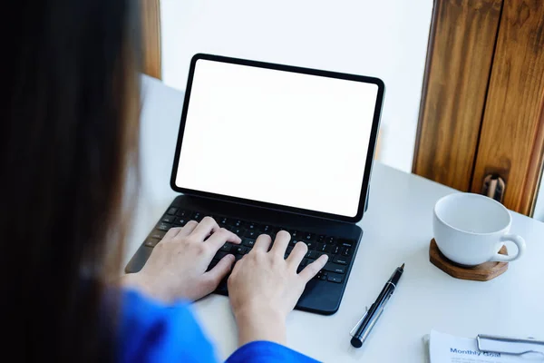 Una mujer de negocios que usa una tableta de pantalla blanca en blanco con una calculadora para calcular documentos presupuestarios en su escritorio — Foto de Stock