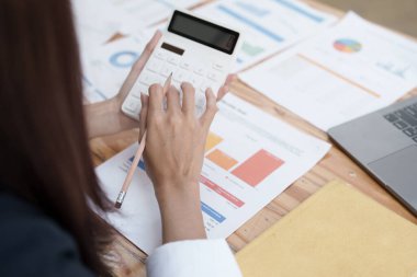 Finansal, Planlama, Pazarlama ve Muhasebe, Asyalı kadın ekonomist, diğer şirketlerle rekabet etmek için ortaklarla yatırım belgeleri hesaplamak için hesap makinesi kullanıyor..