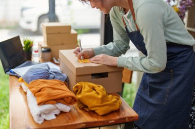 A portrait of a small startup, and SME owner, an Asian female entrepreneur, is writing down information on a notepad to organize the product before packing it into the inner box for the customer.