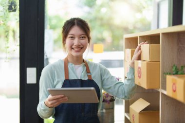 Küçük bir girişimin portresi, bir KME sahibi, bir Asyalı bayan girişimci ürünleri müşterilerle birlikte iç kutulara koymadan önce ürünleri düzenlemek için siparişleri kontrol ediyor. Serbest kavramlar.