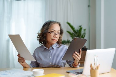 Onaylama için önemli belgeler içeren tablet bilgisayar kullanan yaşlı bir kadının portresi.