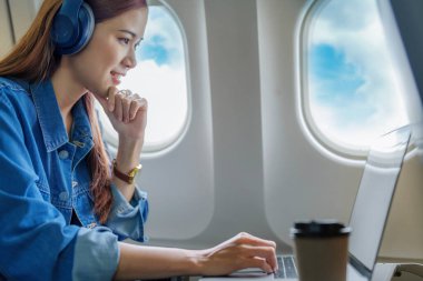Seyahat, gülümseyen Asyalı bir turistin portresi müzik dinlerken ve uçaktayken bilgisayar kullanırken..