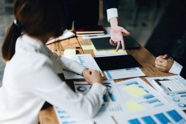 Erkek işadamı, kadın meslektaşlarıyla toplantı, takım çalışması ve yatırım planlamasında pazarlama stratejisini özetleyen belgelere işaret ediyor.