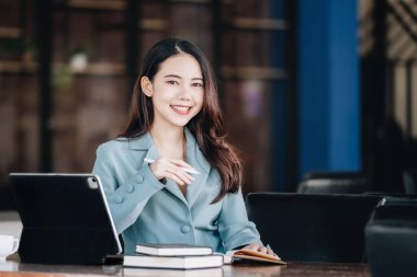 businesswoman showing a smiling face while reading a book developing financial and investing strategies and operating a computer tablet working on a wooden table