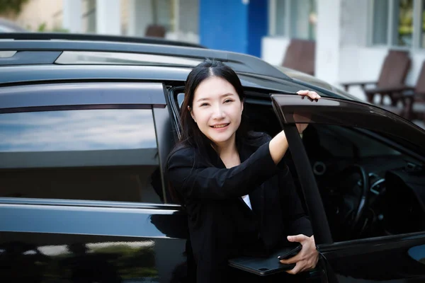 Asian businessmen, business owners, company presidents or female employees holding smartphone mobile and a tablet are getting out of the car to attend a business plan meeting at the meeting