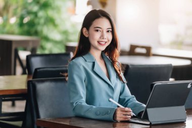 A female entrepreneur or businesswoman showing a smiling face while operating a computer tablet working on a wooden table
