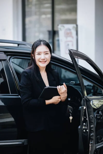 Asian businessmen, business owners, company presidents or female employees holding a tablet are getting out of the car to attend a business plan meeting at the meeting