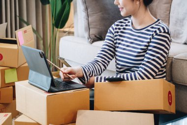 Çevrimiçi iş fikri, evde güzel bir kız tablet bilgisayardaki müşterilerin siparişlerini kontrol ederek ürünleri müşterilere teslim etmek için paket kutusuna koyuyor.