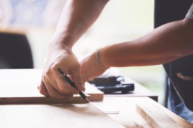 A carpenter measures the planks to assemble the parts, and build a wooden table for the customer.