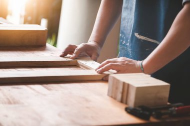 A carpenter measures the planks to assemble the parts, and build a wooden table for the customer