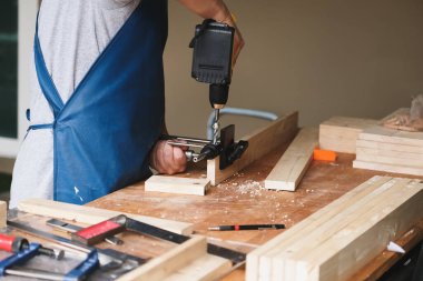 Woodworking entrepreneurs are using a drill through the wood holes to assemble and build wooden tables for customers.