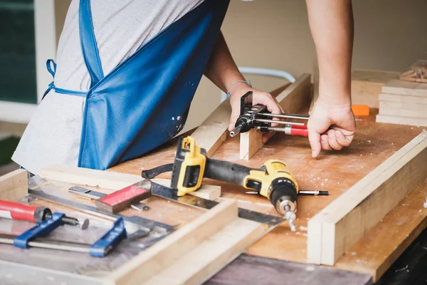 Woodworking operators are using woodworking tools to prepare a drill, drill holes in wood to assemble and build a wooden table for their customers.