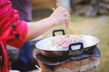 Focus on the pork belly, woman is using chopsticks to hold the pork on the pan