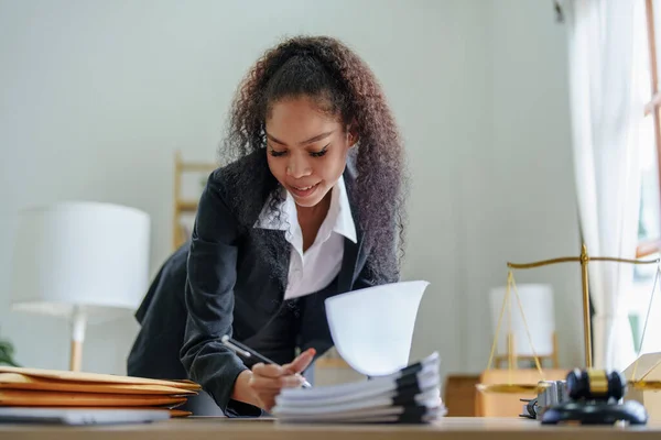 A portrait of an African Americans woman lawyer showing a carefree smiling face is opening a clients document to prepare a court case against the parties