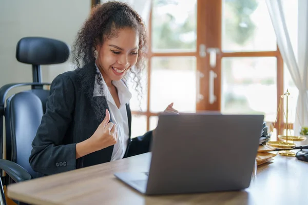 A portrait of a female African Americans lawyer shows joy as she uses a computer after finding a solution to a court case against a client.