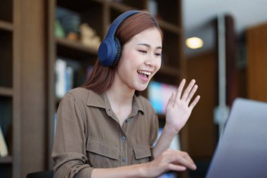 Kulaklık takan, gülümseyen Asyalı genç bir kızın portresi ve bir kütüphanede online video konferansı için bilgisayar kullanımı..