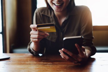 İnternetten alışveriş için kredi kartı ve telefon kullanan Asyalı genç bir kadının portresi..