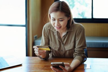 İnternetten alışveriş için kredi kartı ve telefon kullanan Asyalı genç bir kadının portresi..